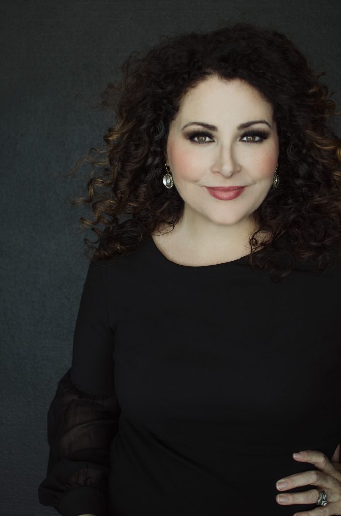 White woman curly hair portrait and headshot photographer standing confidently arm on hip wearing black top and earrings