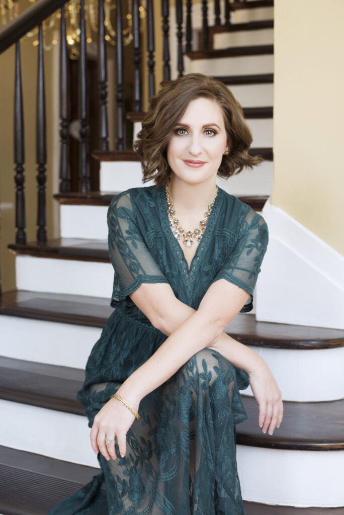 Beautiful smiling white woman with short brown hair wearing a green lace dress arms crossed sitting on staircase