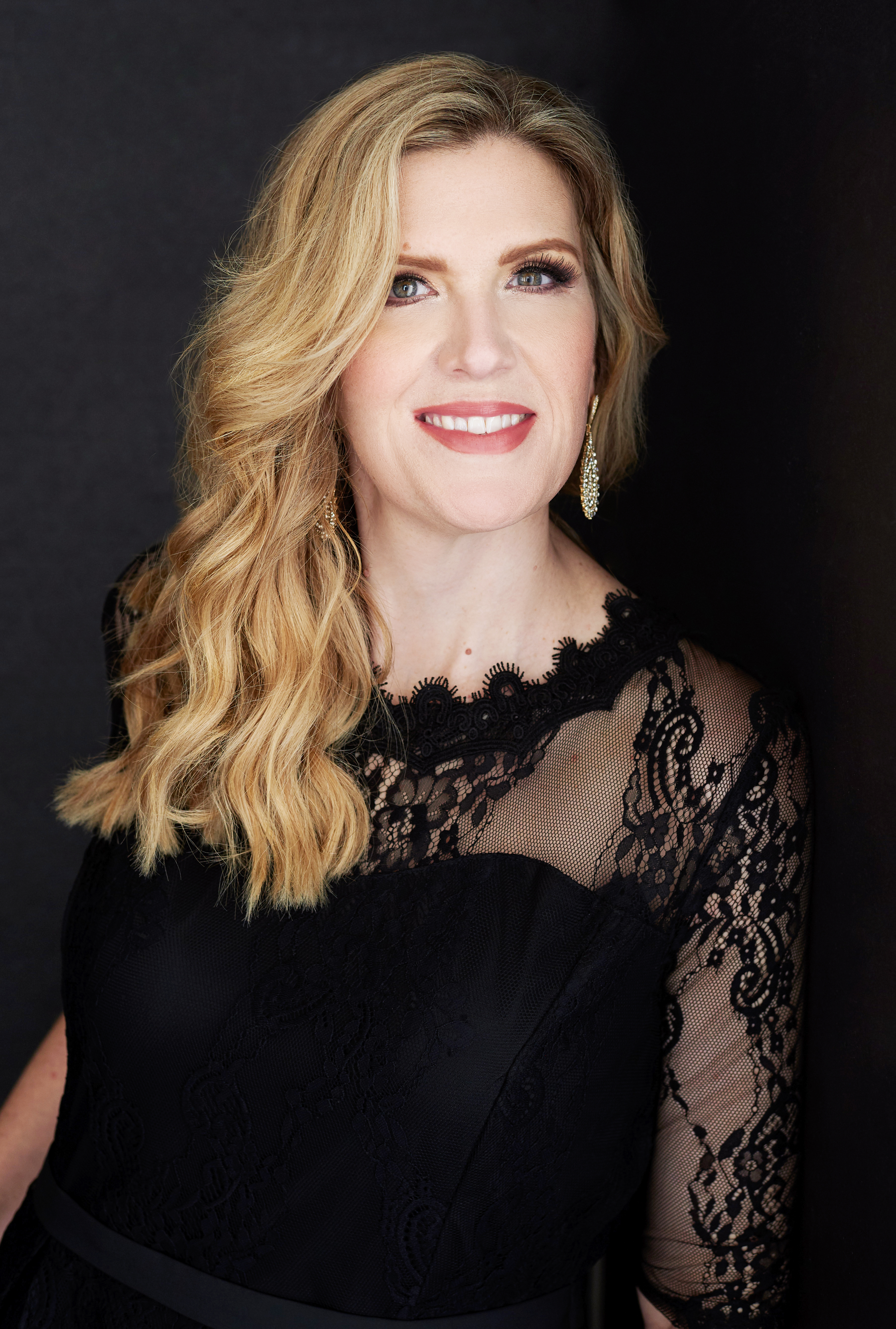 Beautiful smiling white woman with medium wavy blonde hair wearing a black lace top