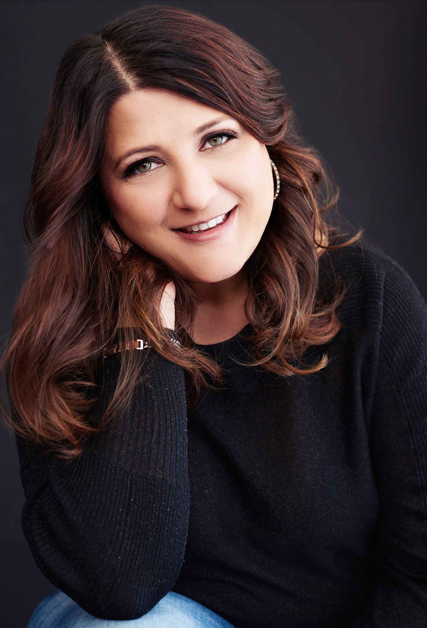 Beautiful smiling white woman with short brunette hair wearing a black sweater and jeans. Professional headshot and glamour shot.