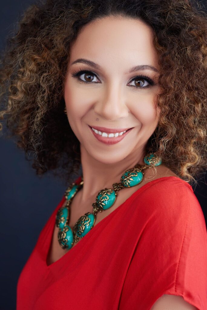 Beautiful smiling woman with curly brown hair wearing a pink blouse. Professional headshot and glamour shot.