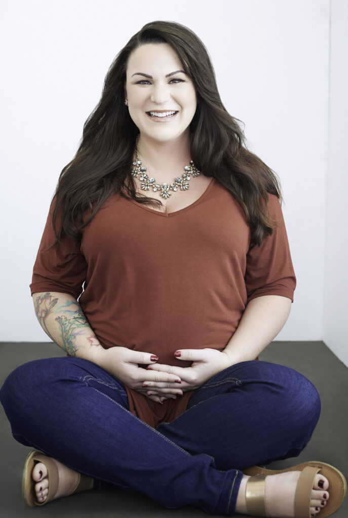 Beautiful smiling brunette woman with tattoos, sitting cross-legged wearing a red shirt and jeans