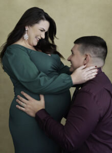 Beautiful pregnant smiling brunette pregnant woman in long green dress hugging husband
