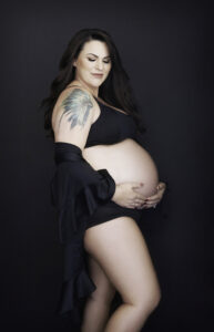 Beautiful brunette pregnant woman in black with exposed belly and tattoos, boudoir maternity
